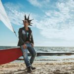 Sänger n-Euro mit spitzen Haaren steht an einem Strand und lehnt an ein rotes Boot
