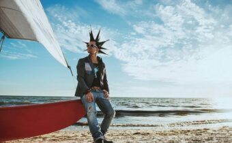 Sänger n-Euro mit spitzen Haaren steht an einem Strand und lehnt an ein rotes Boot