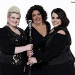 Band BigSoul in schwarzer glitzernder Kleidung, drei Frauen mit kurzen Haaren stehen vor einem Mikrofon 