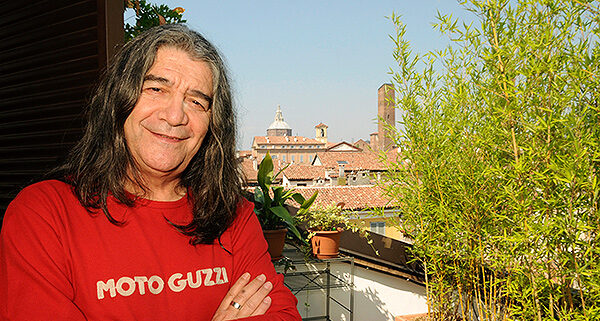 Sänger Drupi steht auf einem Balkon in einem roten Shirt mit langen Haaren