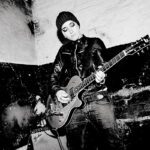 Sängerin Elli spielt E-Gitarre vor einer kahlen Wand, das Bild ist schwarz-weiß