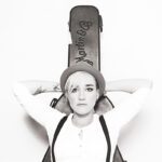 Sängerin Elli in schwarz-weiß lehnt an eine Gitarrentasche, sie trägt einen Hut