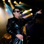 Sänger Falco Forever steht in einem Leder Anzug auf der Bühne und trägt eine Sonnenbrille