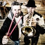 Johanns Erben stehen in einem Festzelt, sie halten Instrumente in der Hand, einer spielt das Saxofon 