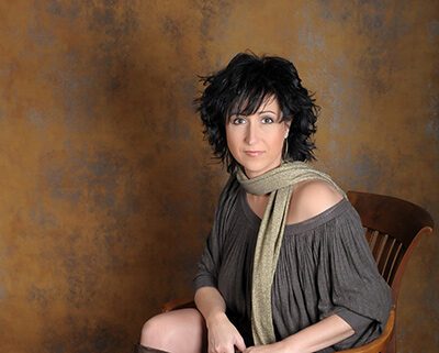 Sängerin Nelly Sander auf einem Stuhl sitzend vor einer Braun grauen Wand