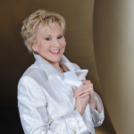 Sängerin Peggy March in silberner glänzender Jacke auf gold grauem Hintergrund